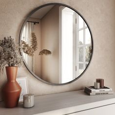 a round mirror is on the wall above a dresser and vase with flowers in it