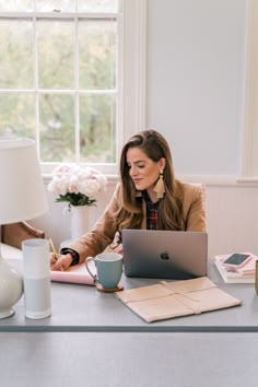 a woman sitting at a desk with a laptop and coffee cup in front of her