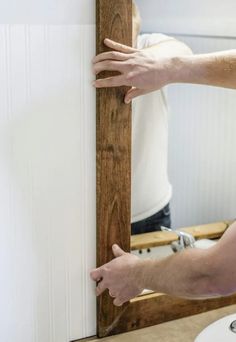 a man that is standing in front of a mirror with his hands on the frame