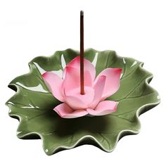 a pink flower sitting on top of a green leaf shaped bowl with a brown stick sticking out of it