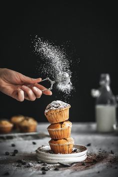 someone sprinkling sugar on top of some muffins