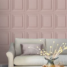 a living room with a couch, coffee table and vase filled with flowers in front of a pink paneled wall