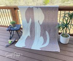 a blanket sitting on top of a wooden deck next to a potted plant and chair