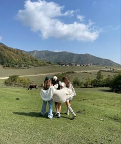 three girls are standing in the grass with their arms around each other and looking at horses