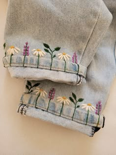 two pairs of jeans with flowers embroidered on the side, sitting next to each other