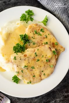 two pieces of chicken covered in gravy and parsley on a white plate