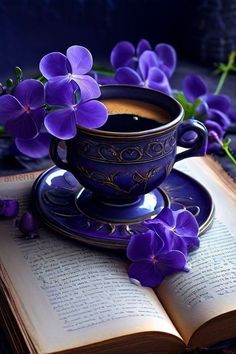 an open book with purple flowers sitting on top of it next to a cup and saucer