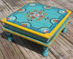 a blue and yellow painted wooden table with flowers on the top, sitting on a wood floor