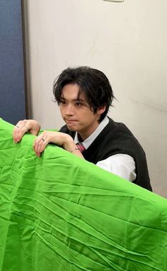 a young man leaning on the edge of a bed with his arm wrapped around an unmade green sheet