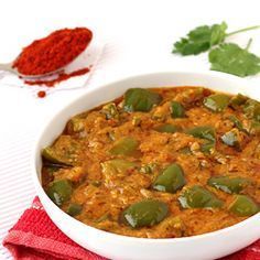 a white bowl filled with curry and green peppers on top of a red napkin next to a spoon