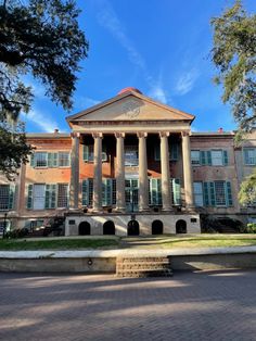 an old brick building with columns and pillars on the front, surrounded by greenery