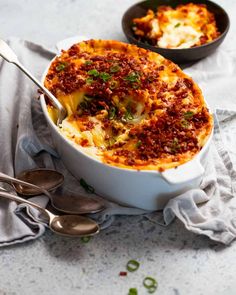 a casserole dish with meat and cheese in it next to two spoons