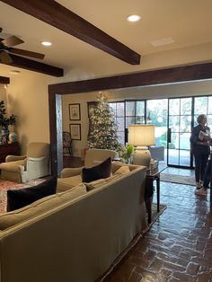 a living room filled with furniture and a woman standing in front of a window next to a christmas tree