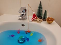 a bathtub filled with blue water and goldfish under a faucet next to christmas trees