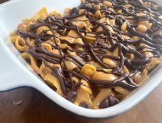 a white dish filled with lots of chocolate and macaroni shells on top of a wooden table