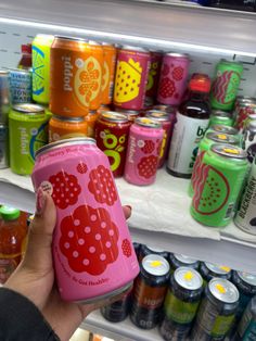 a person is holding up a can of soda in front of a refrigerator full of soft drinks