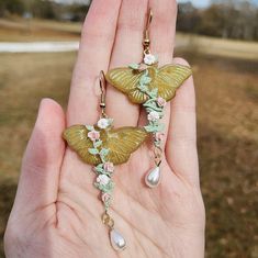 A pair of earrings featuring a luna moth, sculpted from translucent polymer clay and shaded with chalk pastels. The moth is wrapped up in an arrangement of clay vines, leaves, roses and daisies. ✨️🌷 Roses And Daisies, Translucent Polymer Clay, Moth Earrings, Vines Leaves, The Moth, Luna Moth, Pigment Powder, Chalk Pastels, Cute Sets