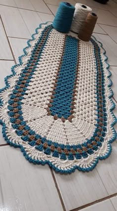 a blue and white crocheted rug on the floor next to a roll of yarn