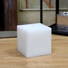 a white square candle sitting on top of a wooden table