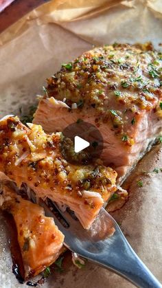 a piece of salmon with herbs on it and a fork in the foreground, sitting on top of parchment paper