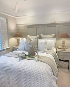 a bed with white comforter and pillows in a bedroom next to two lamps on either side of the bed