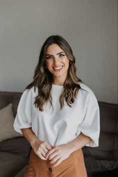 a woman standing in front of a couch with her hands on her hips and smiling