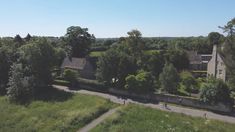 an aerial view of a country house surrounded by trees and people riding bikes on the road