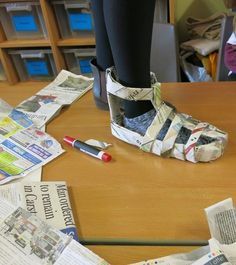 a person standing on top of a wooden table next to newspaper and a red pen