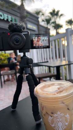 a cup of coffee sitting on top of a table next to a tripod with a camera