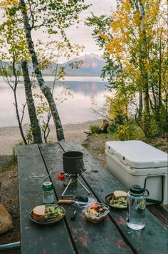 a picnic table with food on it next to the water