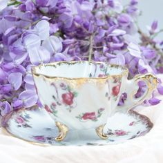 a tea cup and saucer with purple flowers in the background