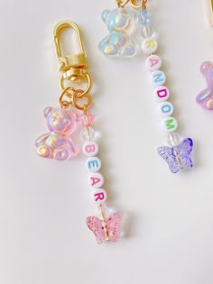 three keychains with letters and butterflies attached to them, on a white surface