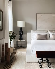 a white bed sitting in a bedroom next to a mirror and table with two lamps on it