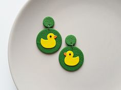 two green and yellow earrings with rubber ducks on them are sitting on a white plate