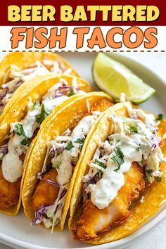 three fish tacos on a white plate with lime wedges