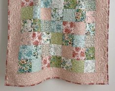 a pink and green quilt hanging on a wall