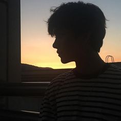 a man standing in front of a window with the sun setting behind him and his hair blowing back