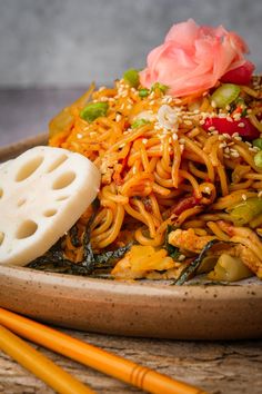 a plate full of noodles and vegetables with chopsticks