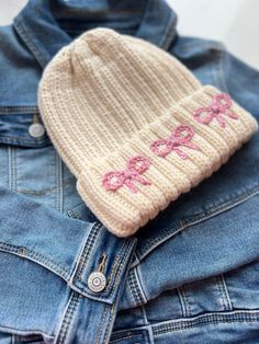 a white knitted hat with pink bows on it sitting on top of a jean jacket