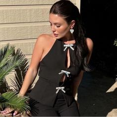 a woman in a black dress is sitting on a chair outside with palm trees and potted plants behind her