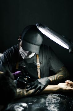 a man with tattoos on his arm and wearing a black hat, holding a knife