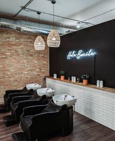 the interior of a barbershop with black chairs and white sinks in front of a brick wall