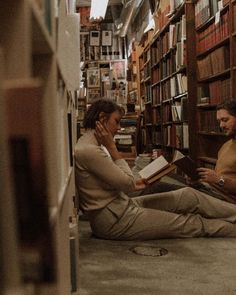 two people are sitting on the floor in a library reading books and talking on their cell phones