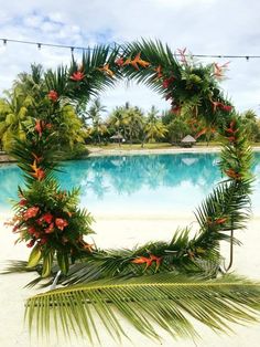 a tropical wreath made out of palm leaves and red flowers on the edge of a pool