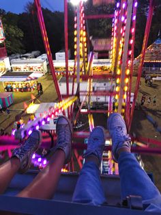 two people sitting on a carnival ride with their feet up in the air at night