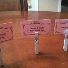 three pieces of pink paper on top of a wooden table with name tags attached to them