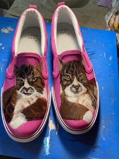 a pair of pink shoes with a cat painted on the side and green eyes, sitting on a blue surface