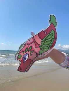 a person holding up a cut out of a fish on the sand at the beach