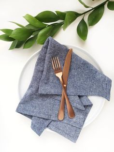 a white plate topped with silverware next to a green leafy plant on top of it