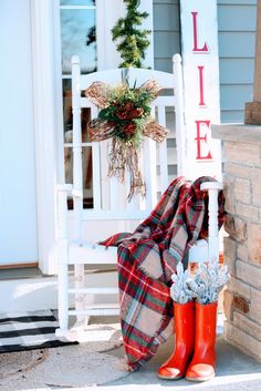 a white rocking chair sitting on top of a porch next to a christmas wreath and red rubber boots